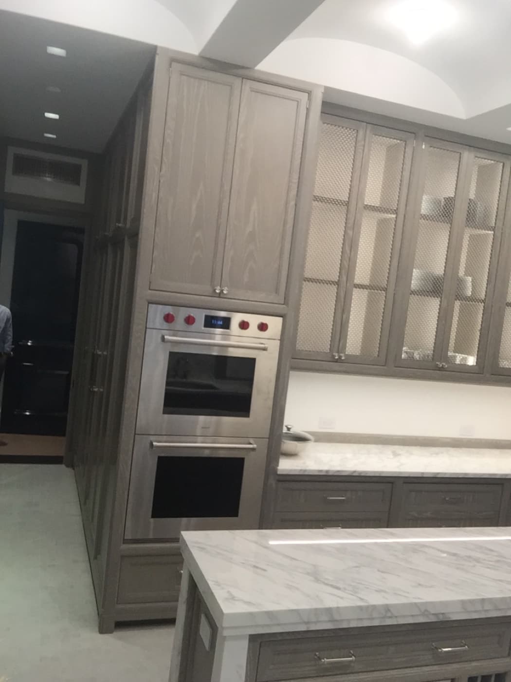Kitchen featuring grey-toned wood cabinetry, built-in double ovens, and pale veined stone countertops