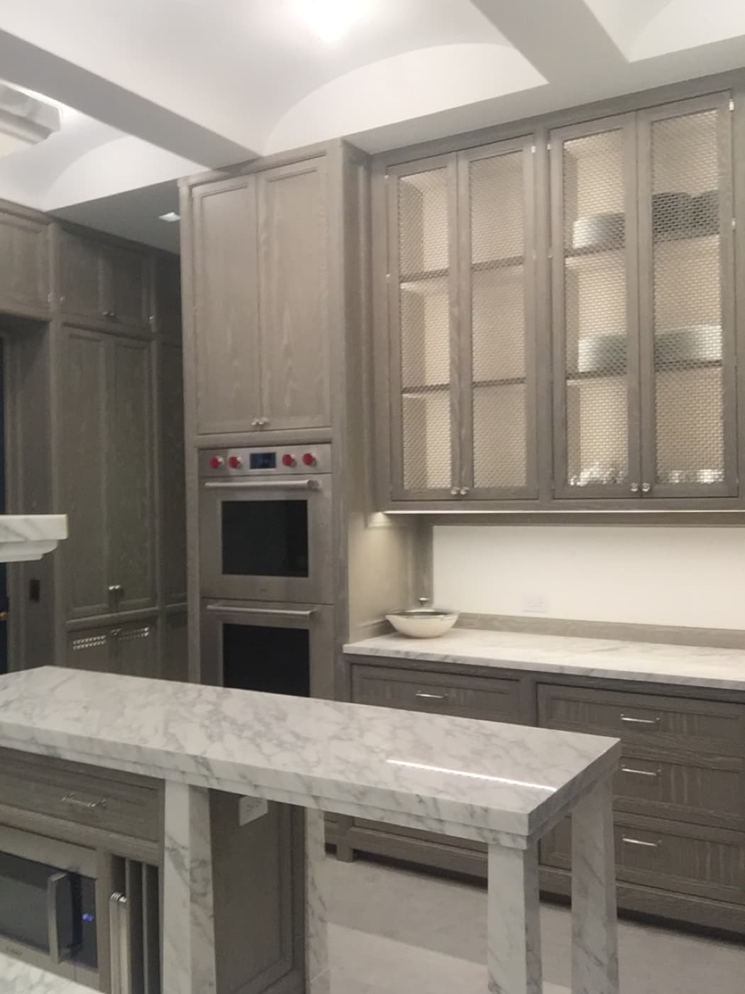 Kitchen featuring grey timber cabinetry with wire mesh upper doors and pale veined stone countertops