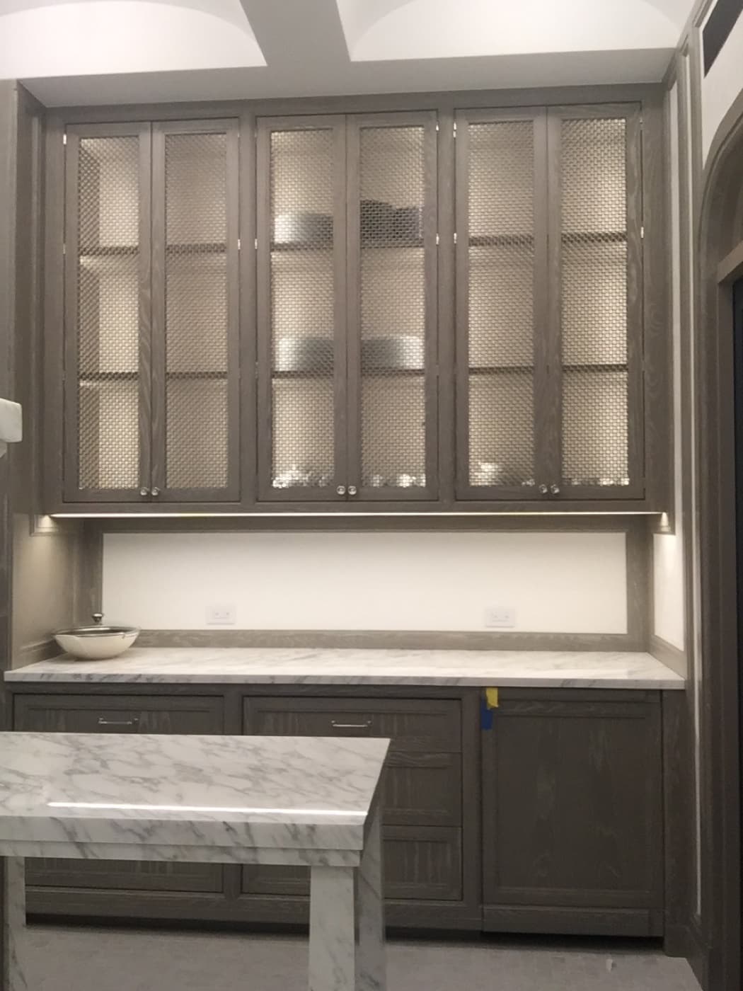 Butler's pantry cabinetry with wire mesh upper doors and pale veined stone countertops