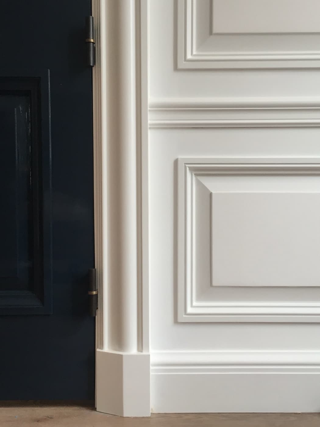 Interior doorway showing white raised wall panelling, detailed casing trim, and dark paneled door
