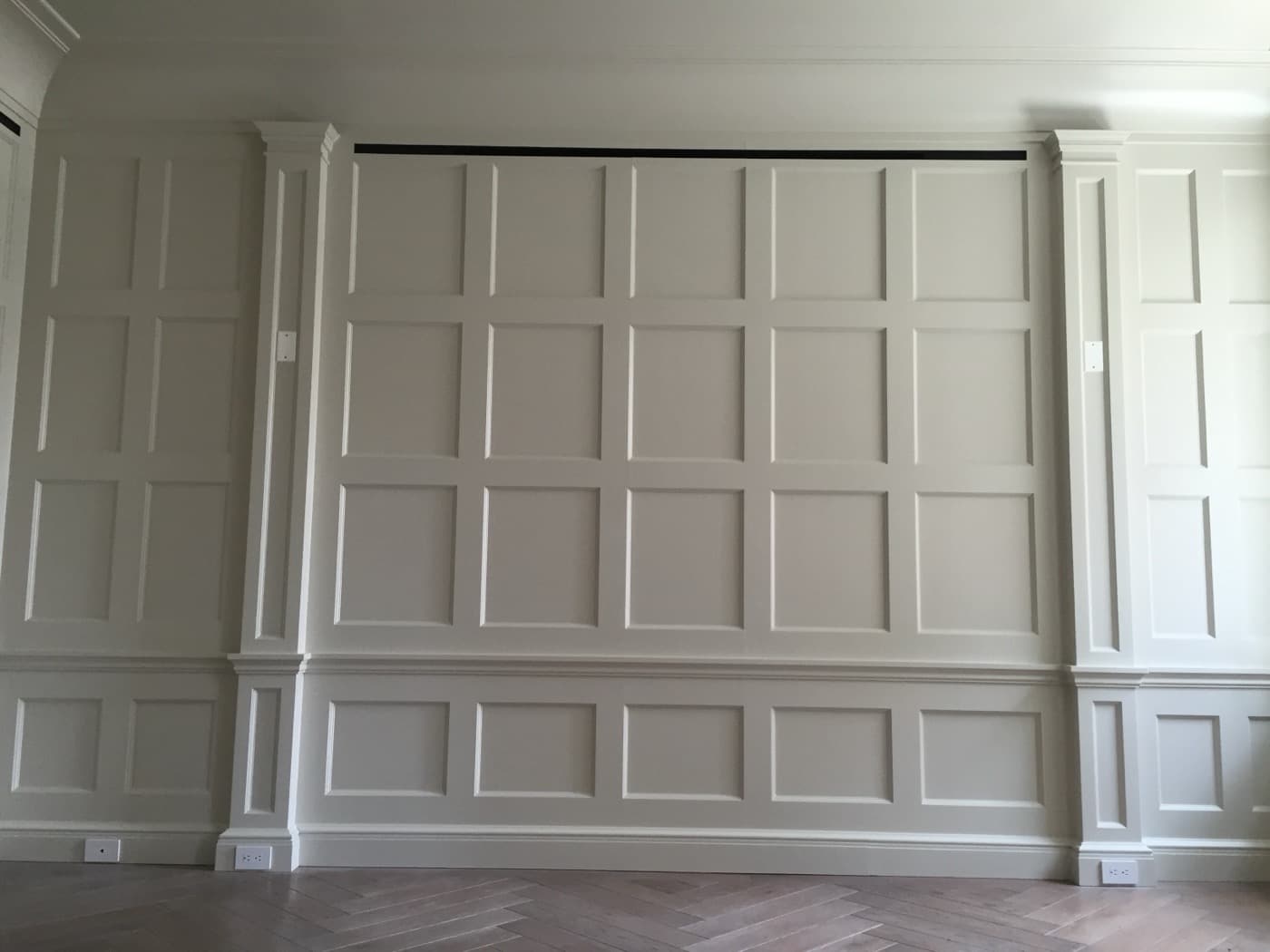 Interior room featuring full-height painted wall panelling with flanking pilasters and herringbone timber flooring