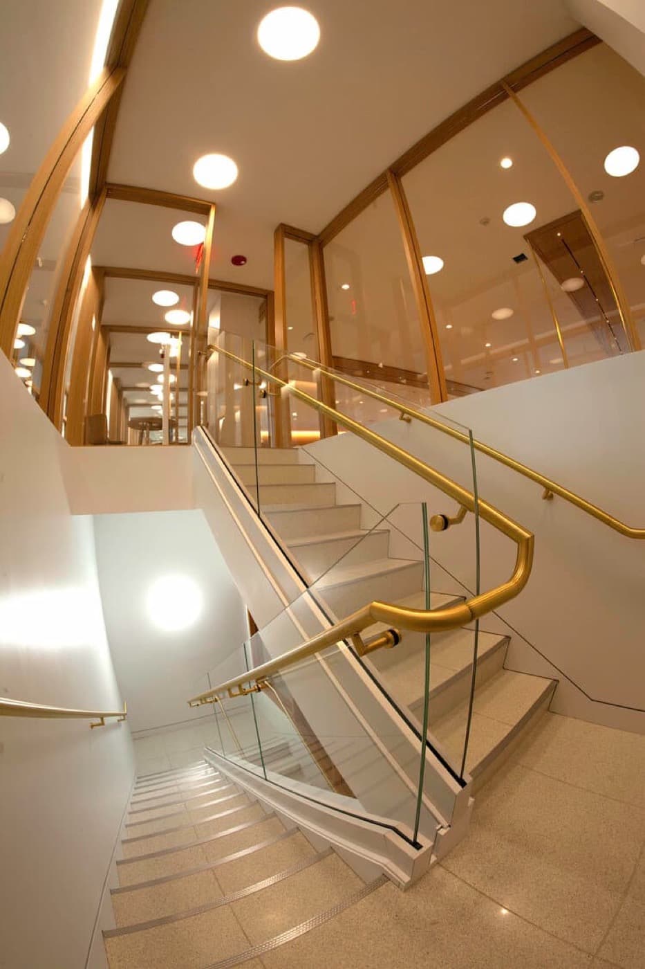 Modern office staircase with glass balustrades, brass handrails, and timber-framed glazed partitions above