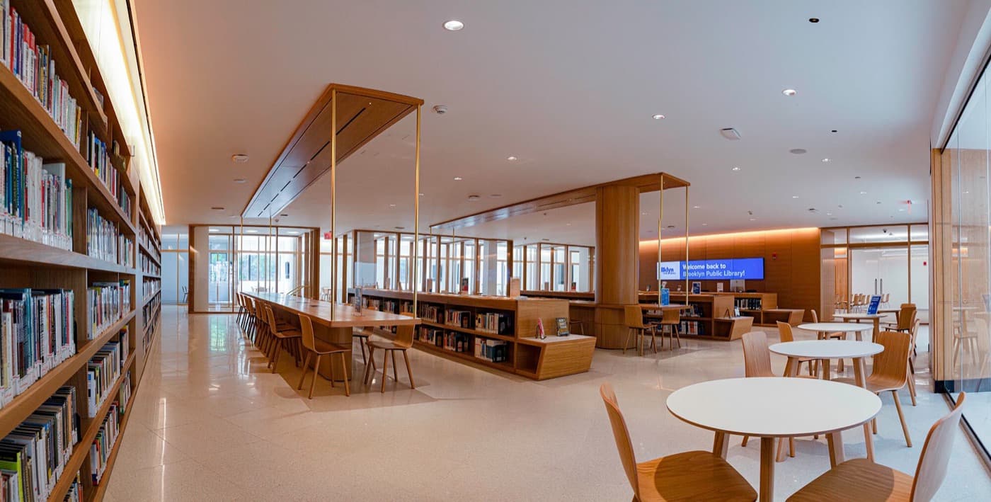 Library reading room with custom timber bookcases, integrated communal tables, and overhead millwork canopy