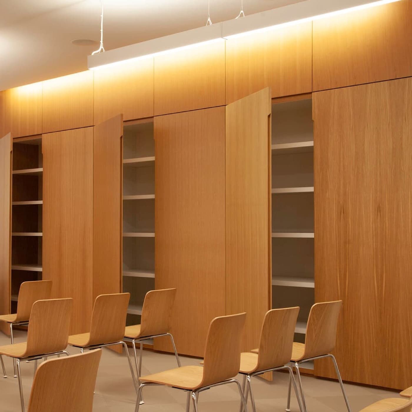 Meeting room featuring full-height warm timber cabinetry with bi-fold doors revealing interior shelving