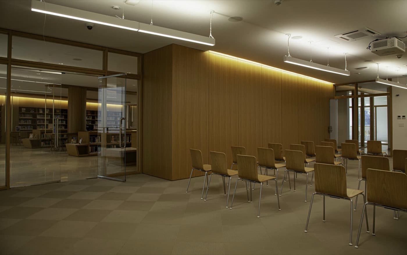 Presentation space featuring illuminated wood-toned wall panelling, glass partition doors, and rows of seating