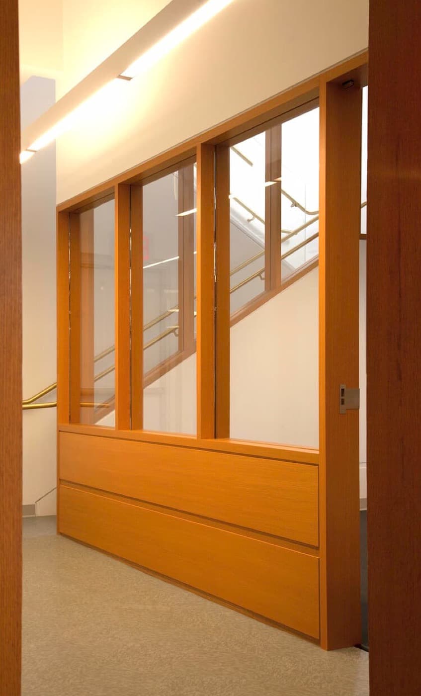 Hallway featuring warm-toned timber and glass partition wall alongside an interior staircase