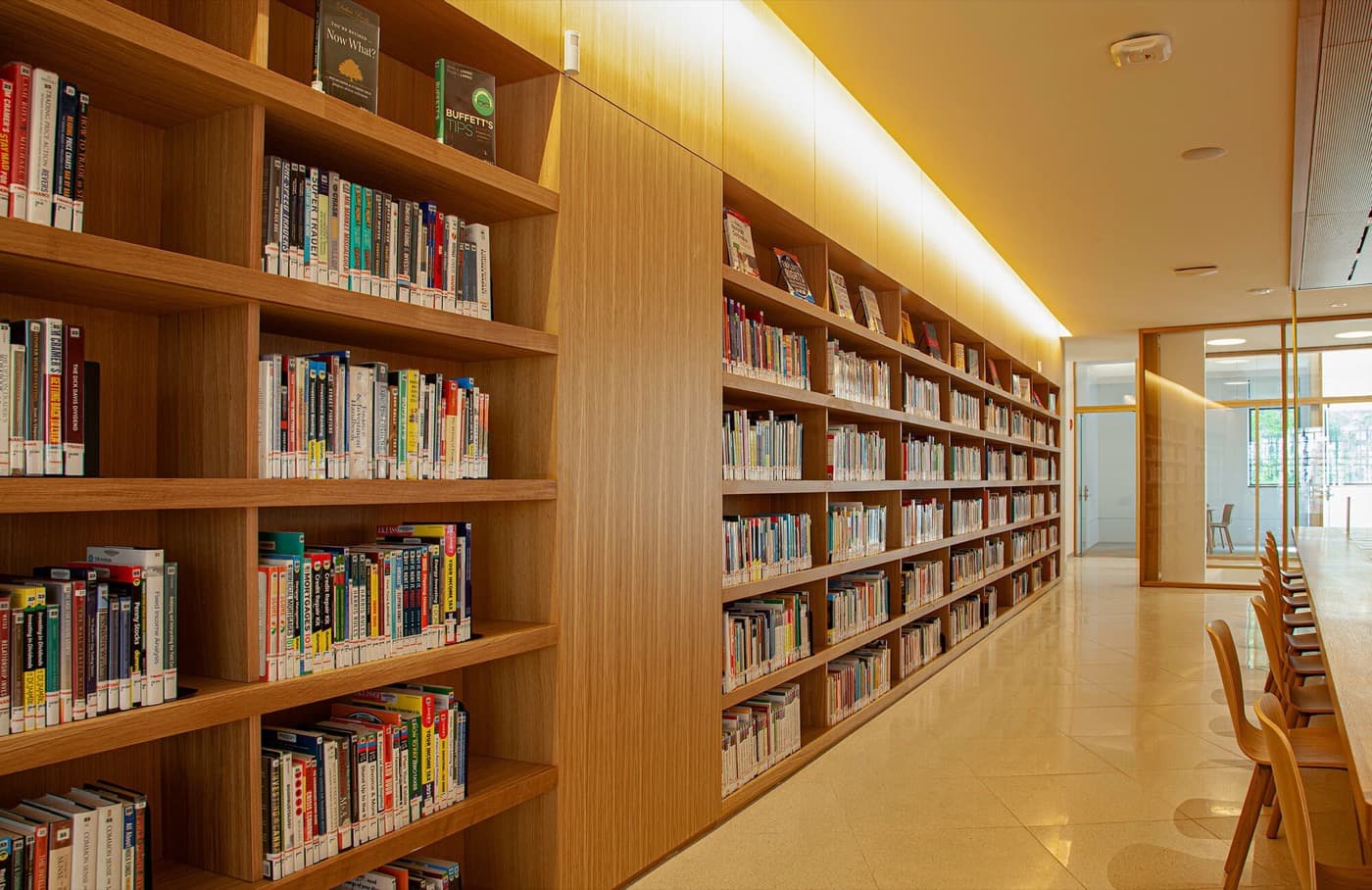 Library with floor-to-ceiling warm timber built-in bookcases, integrated cove lighting, and polished stone flooring