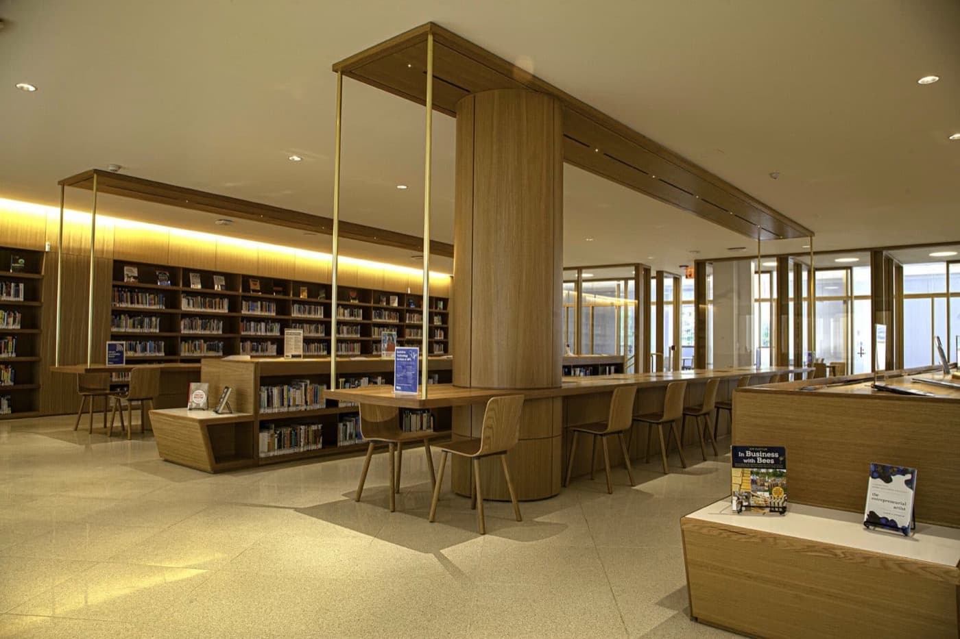 Library with built-in timber study tables, wood-clad structural column, and matching illuminated bookshelves