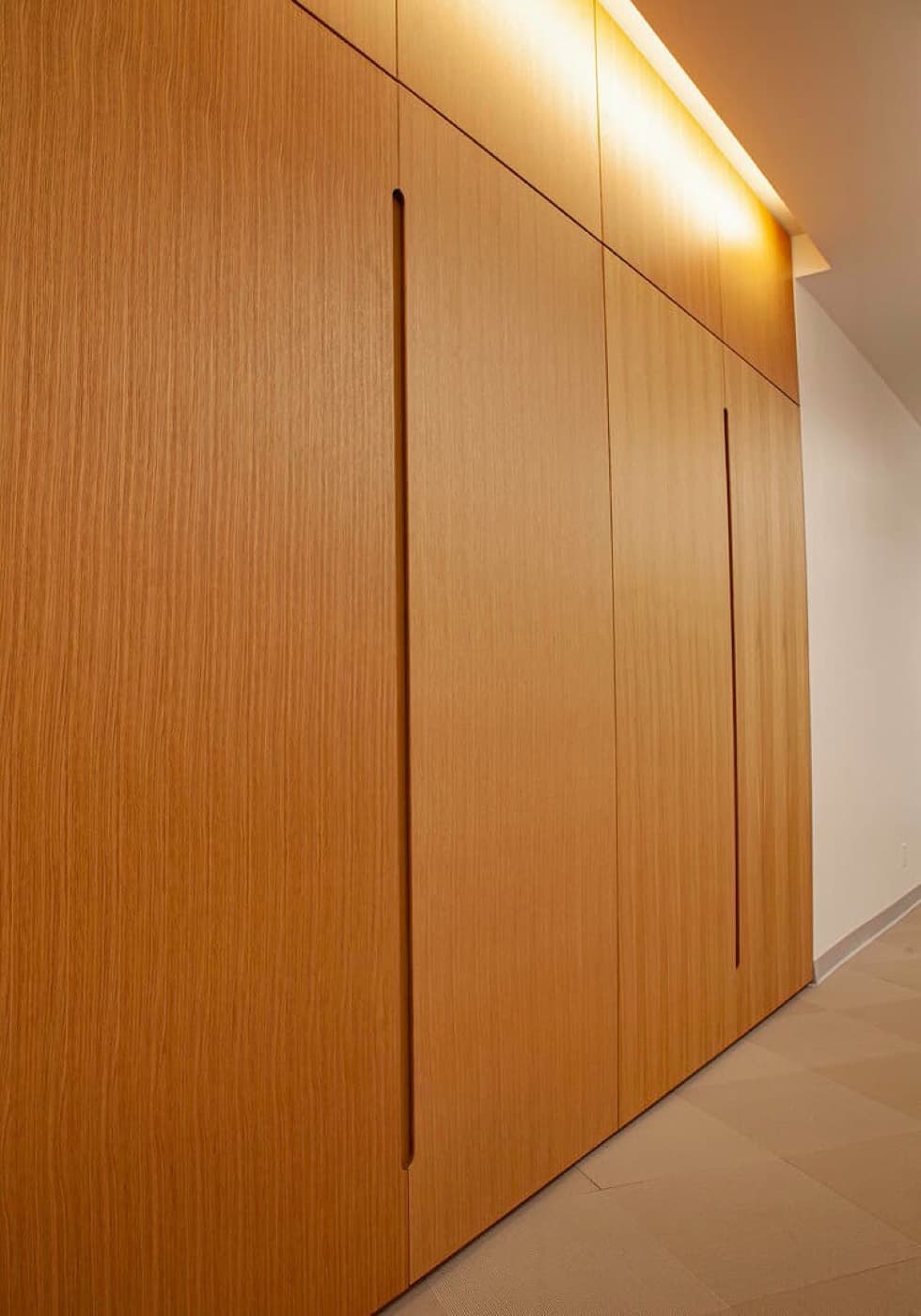 Hallway featuring full-height warm wood-toned cabinetry with integrated recessed pulls and cove lighting