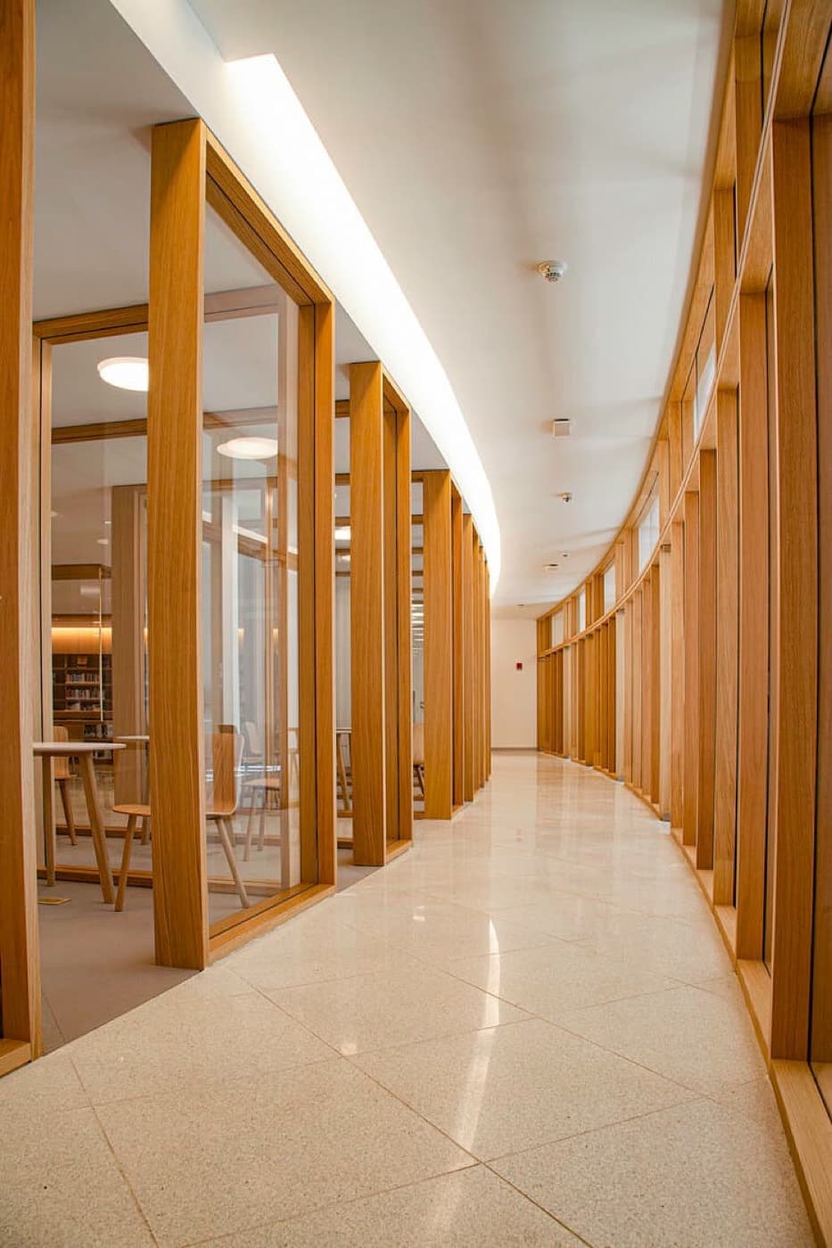 Curved hallway lined with timber and glass partitions beside a polished stone floor