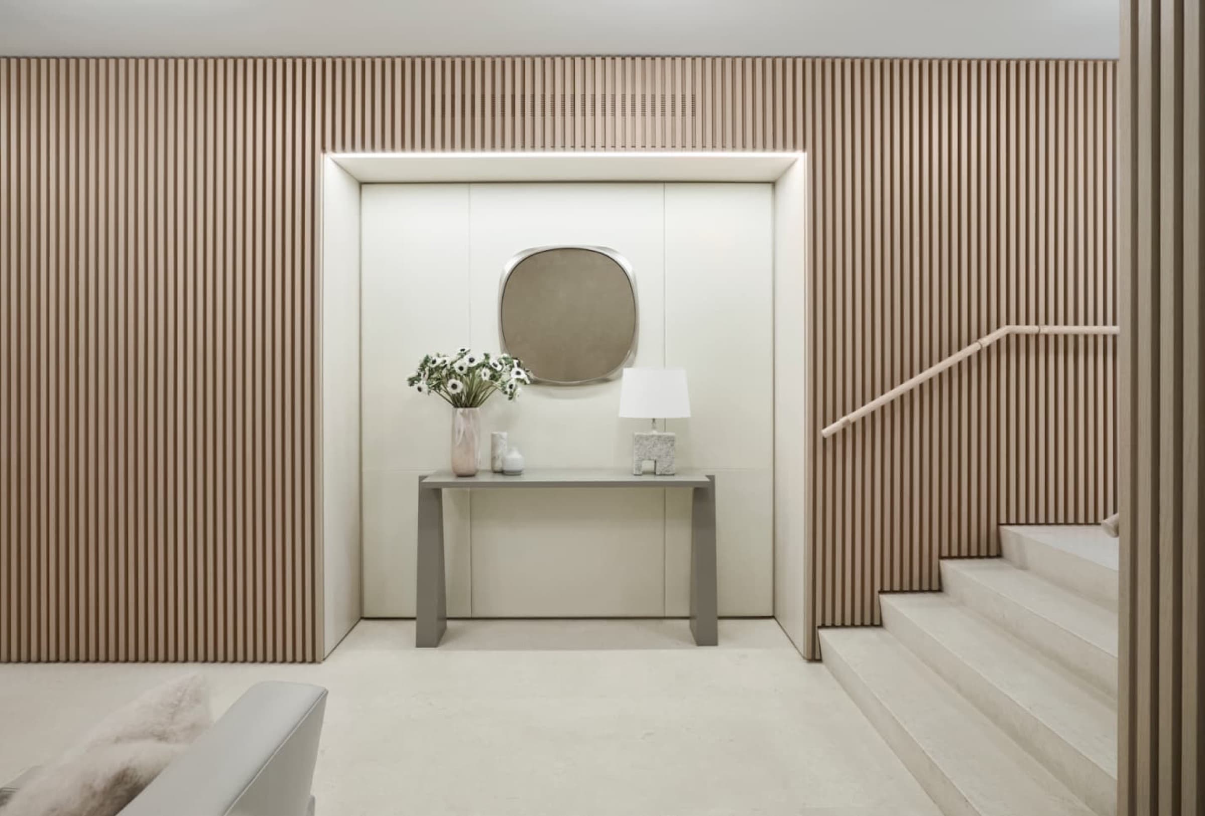 Foyer with vertical timber slat wall panelling, recessed niche, and pale stone staircase