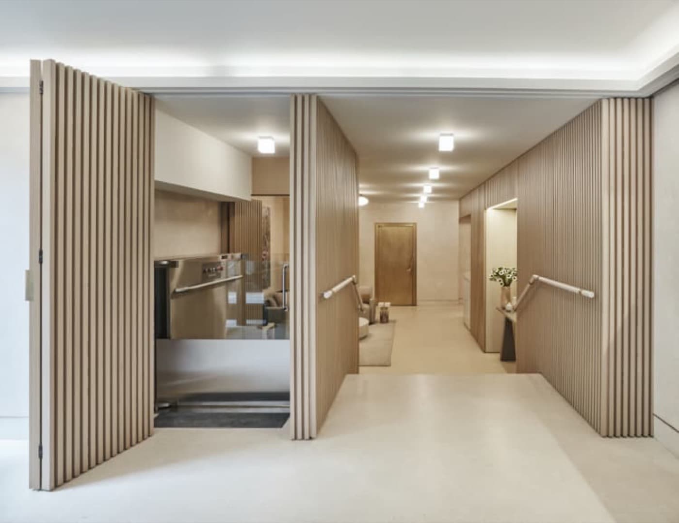 Entryway ramp featuring pale timber slatted wall panelling, handrails, and an accessible platform lift