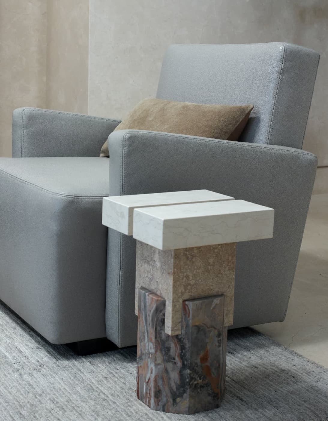 Sitting area with a sculptural multi-toned stone side table beside an upholstered armchair