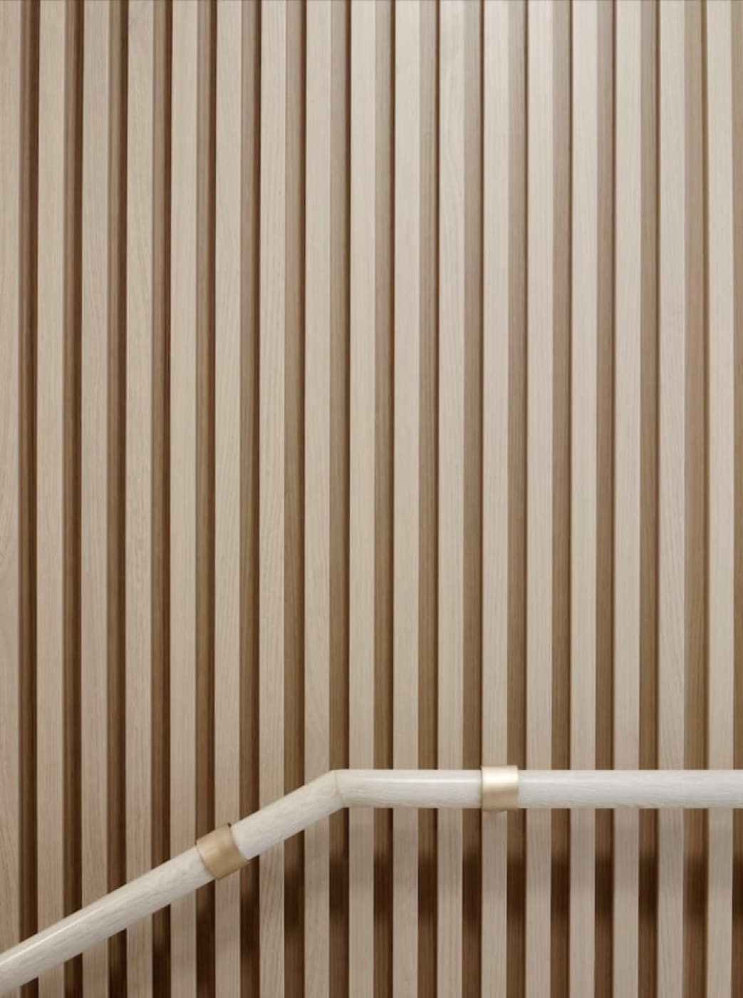 Staircase wall featuring vertical timber slat panelling with a pale handrail and brass-toned fittings