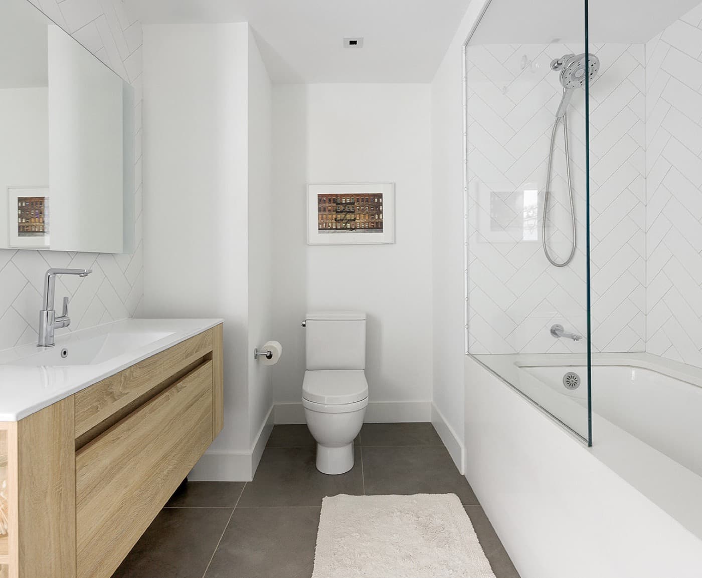 Bathroom featuring a floating light timber vanity and glass-partitioned bathtub with herringbone tile