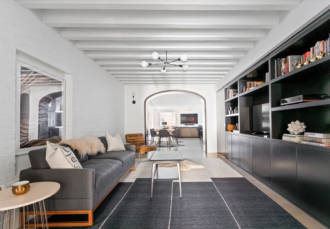 Living room with dark built-in shelving, white painted ceiling beams, and an arched entryway