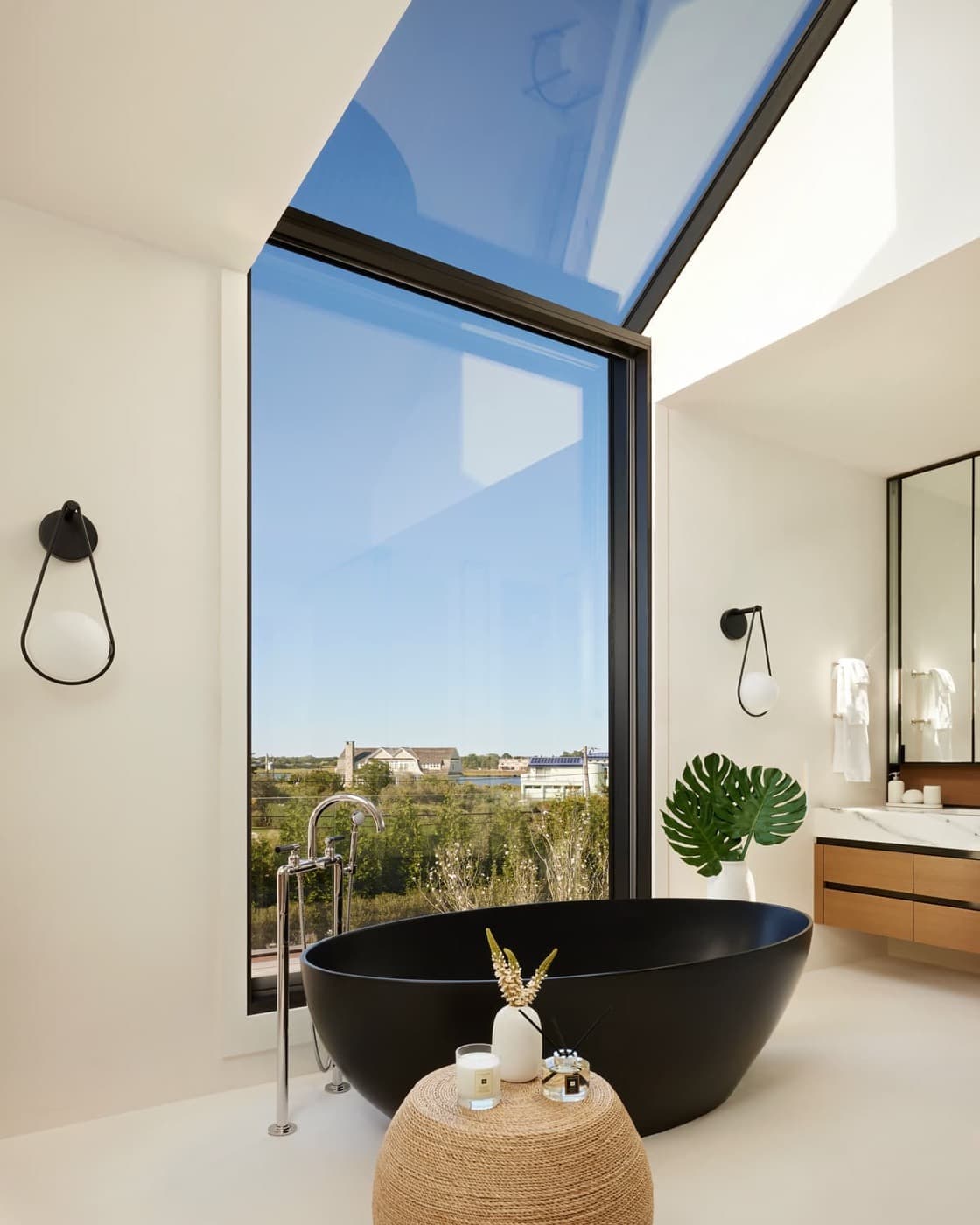 Bathroom with a matte black freestanding bathtub, tall skylight window, and floating timber vanity