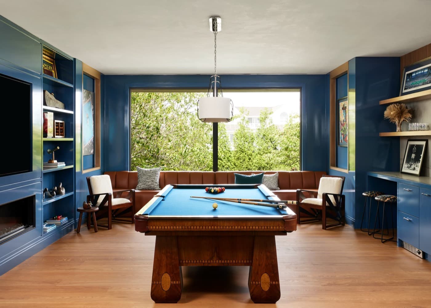 Game room with blue built-in cabinetry, window banquette, and a central timber pool table