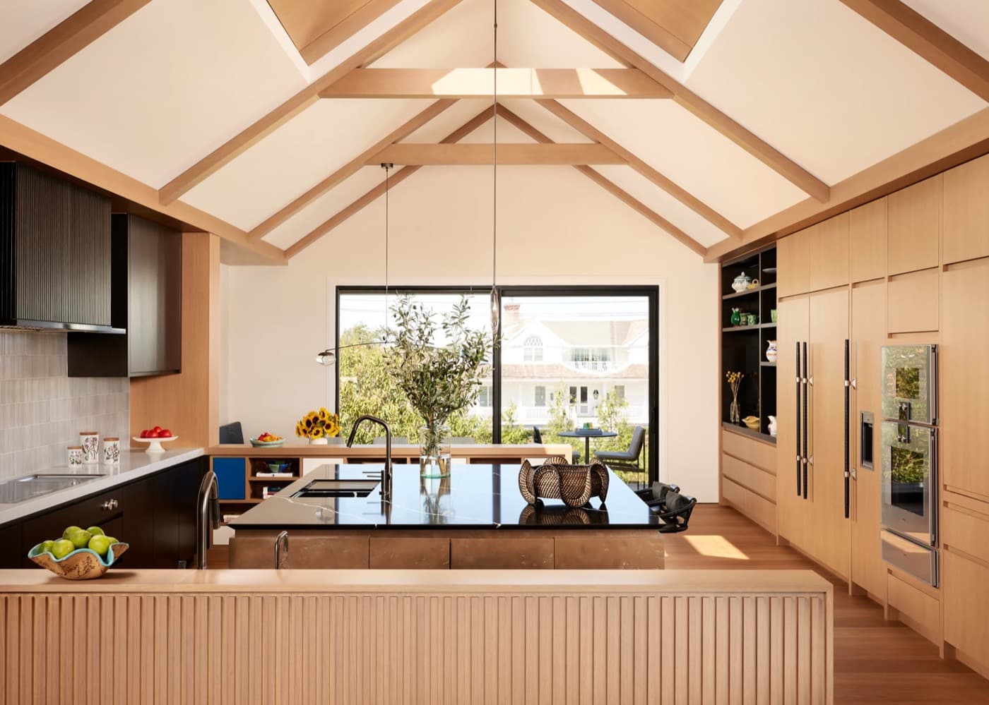Kitchen with a timber-beamed vaulted ceiling, dark stone island, and full-height pale timber cabinetry