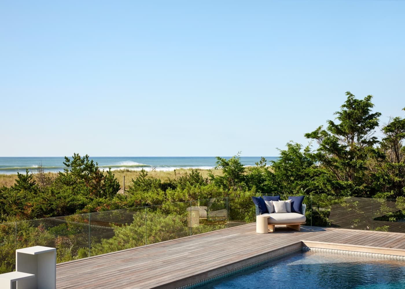 Outdoor pool deck with timber decking and frameless glass railing overlooking the ocean