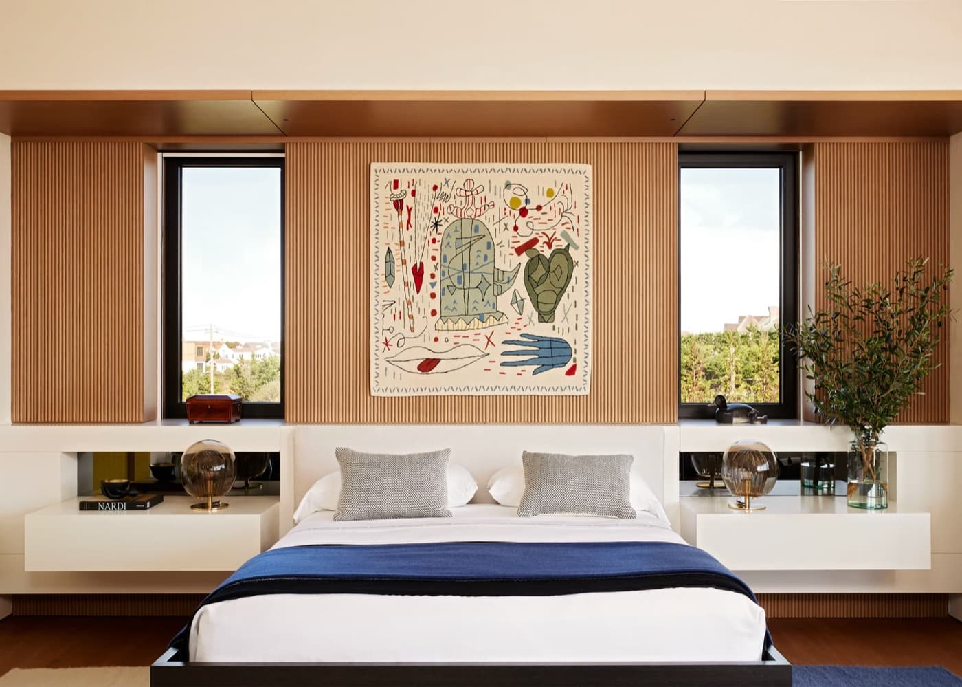 Bedroom featuring fluted timber wall panelling, built-in floating white nightstands, and flanking windows