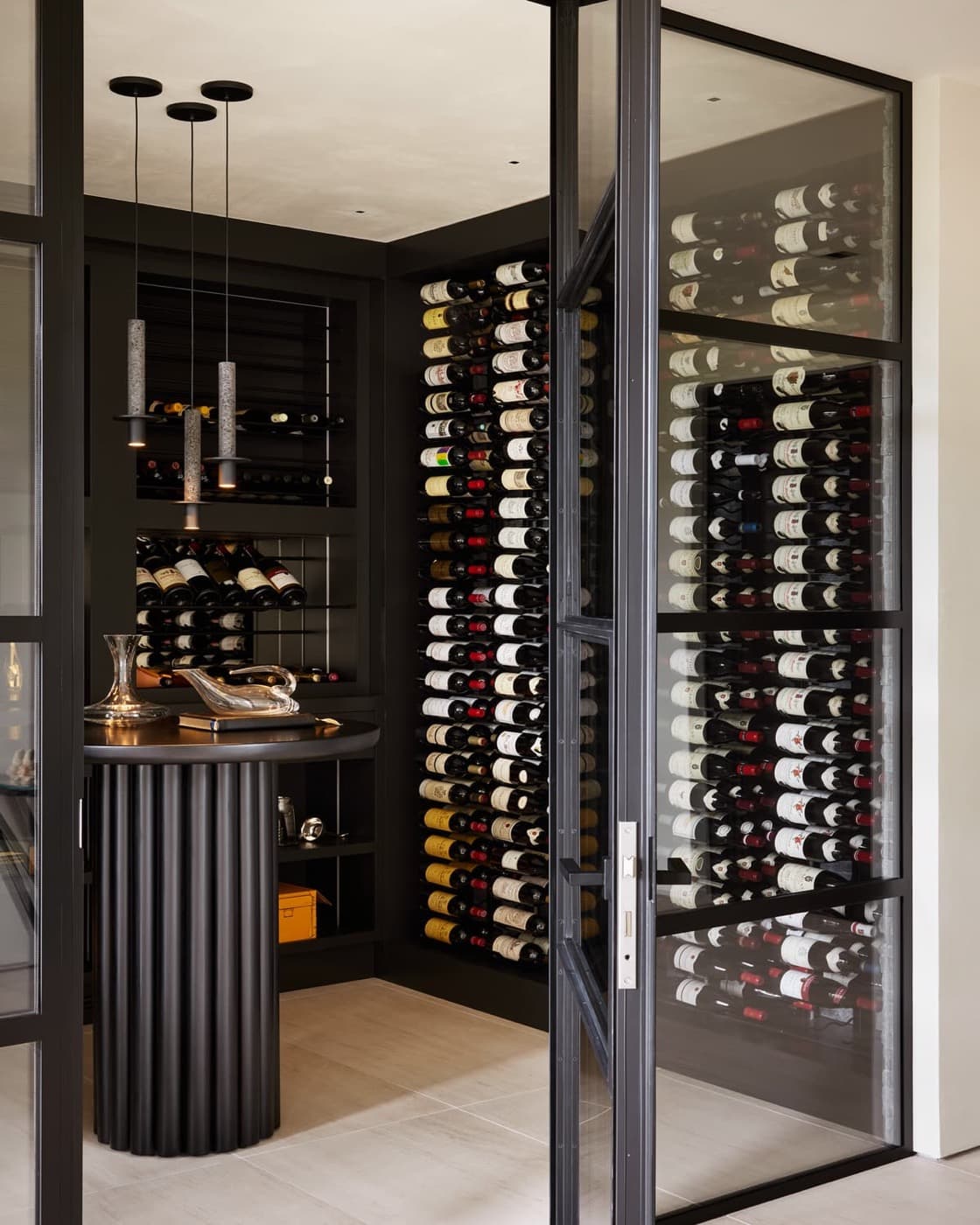Wine cellar with custom dark bottle racking, fluted tasting table, and glazed metal doors