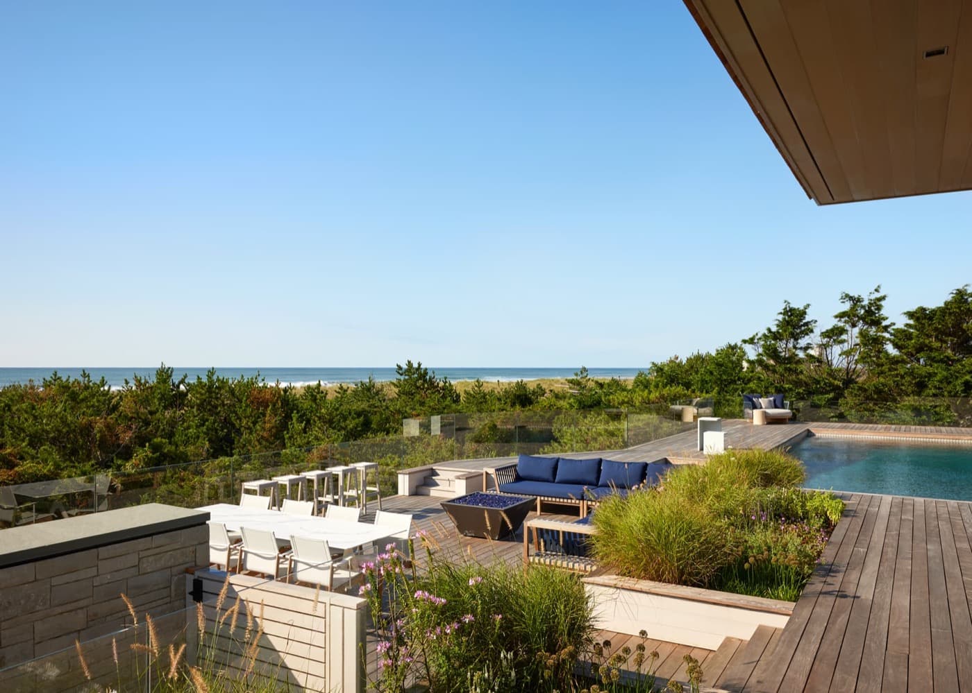 Tiered outdoor timber deck with swimming pool, built-in planters, and oceanfront lounge seating