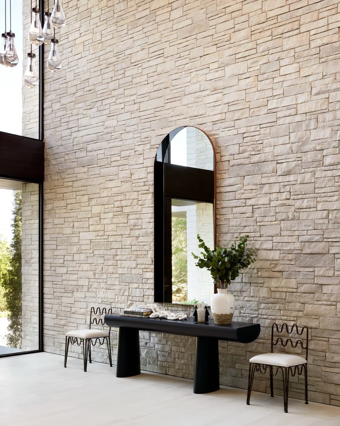 Foyer with a double-height textured pale stone wall, arched mirror, and dark console table