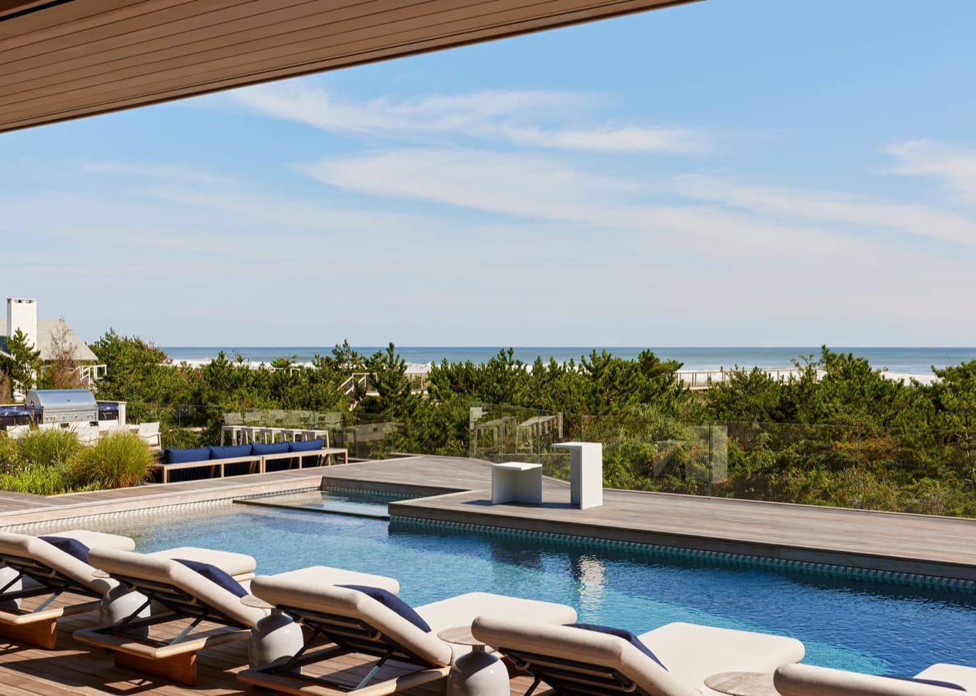 Outdoor pool deck with timber decking, swimming pool, and lounge seating overlooking the ocean