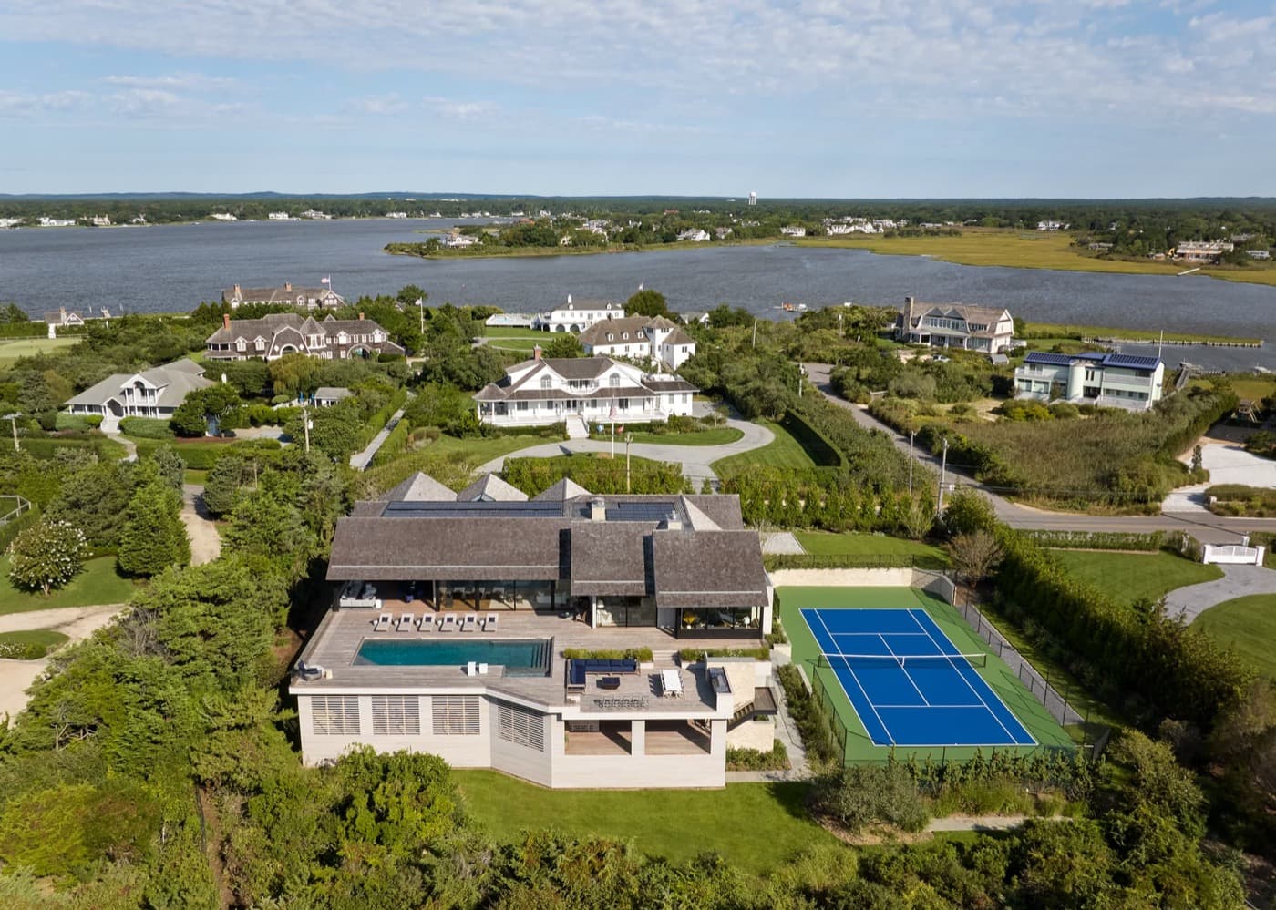 Aerial view of coastal estate with elevated timber deck, swimming pool, and tennis court