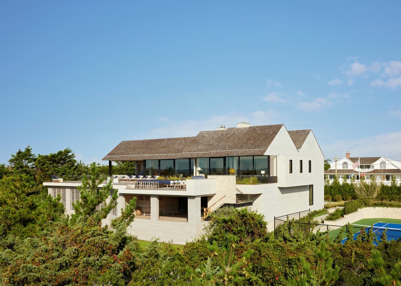 Modern residence exterior featuring wood-shingled gabled roofs, floor-to-ceiling glazing, and elevated outdoor terrace