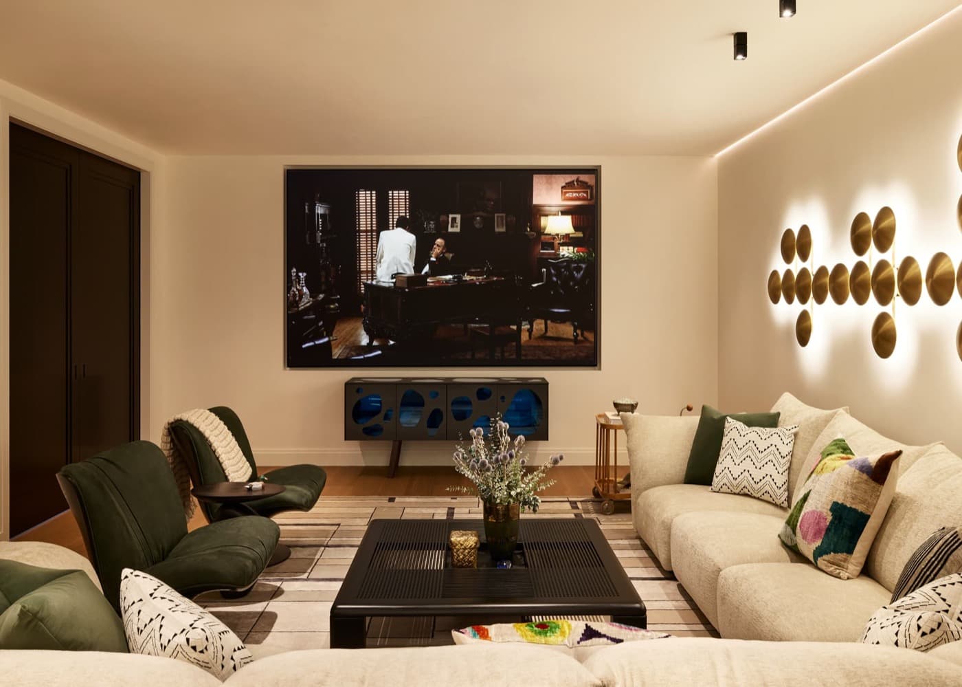Media room featuring upholstered seating, large wall-mounted screen, and sculptural metallic wall sconces