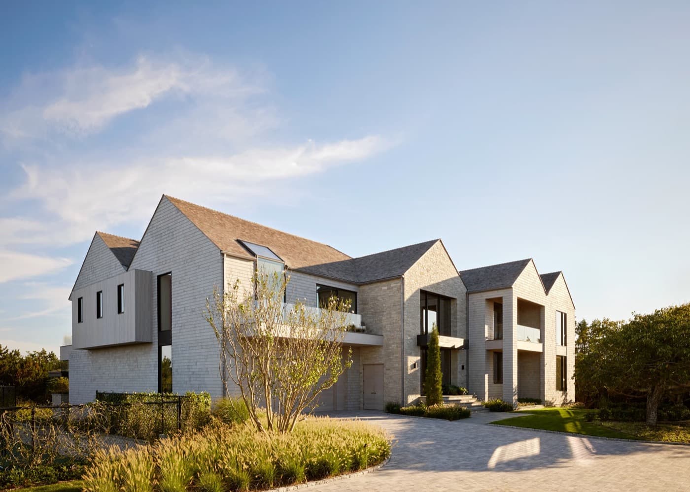 Modern house exterior featuring multiple gabled rooflines, light-toned shingle cladding, and paved driveway