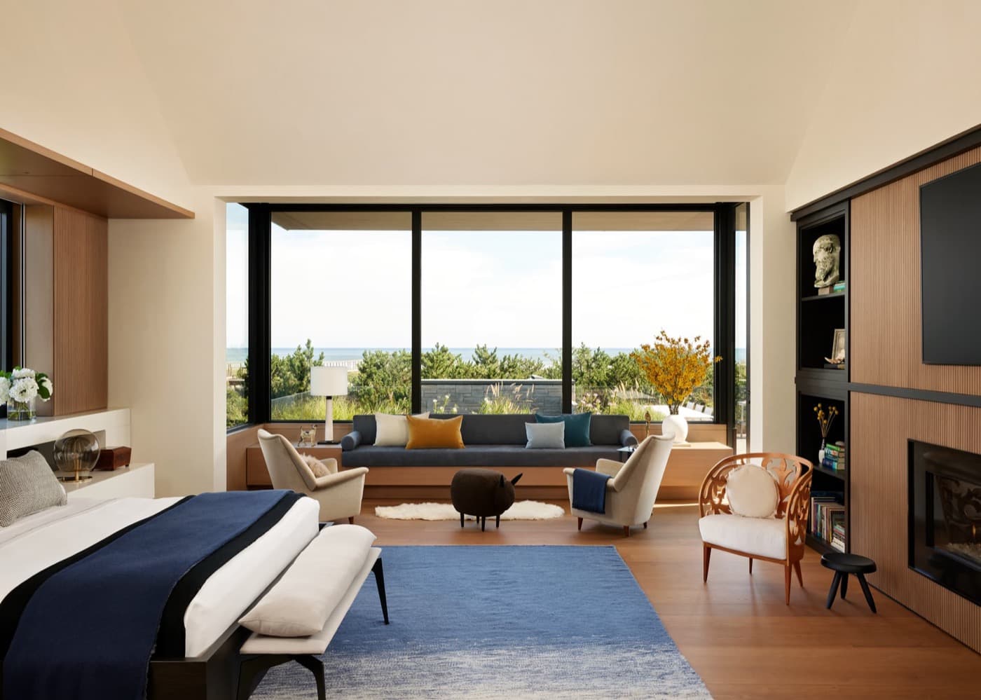Modern bedroom suite with warm timber wall panelling, built-in fireplace, and panoramic window bench