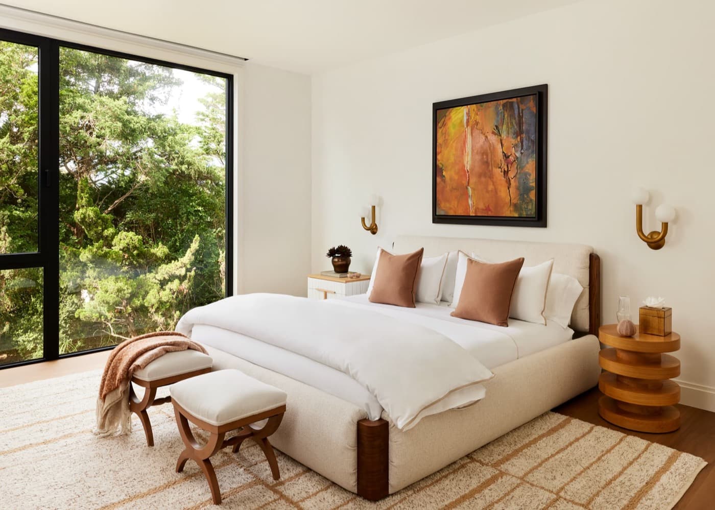 Modern bedroom featuring large dark-framed windows overlooking greenery and an upholstered bed