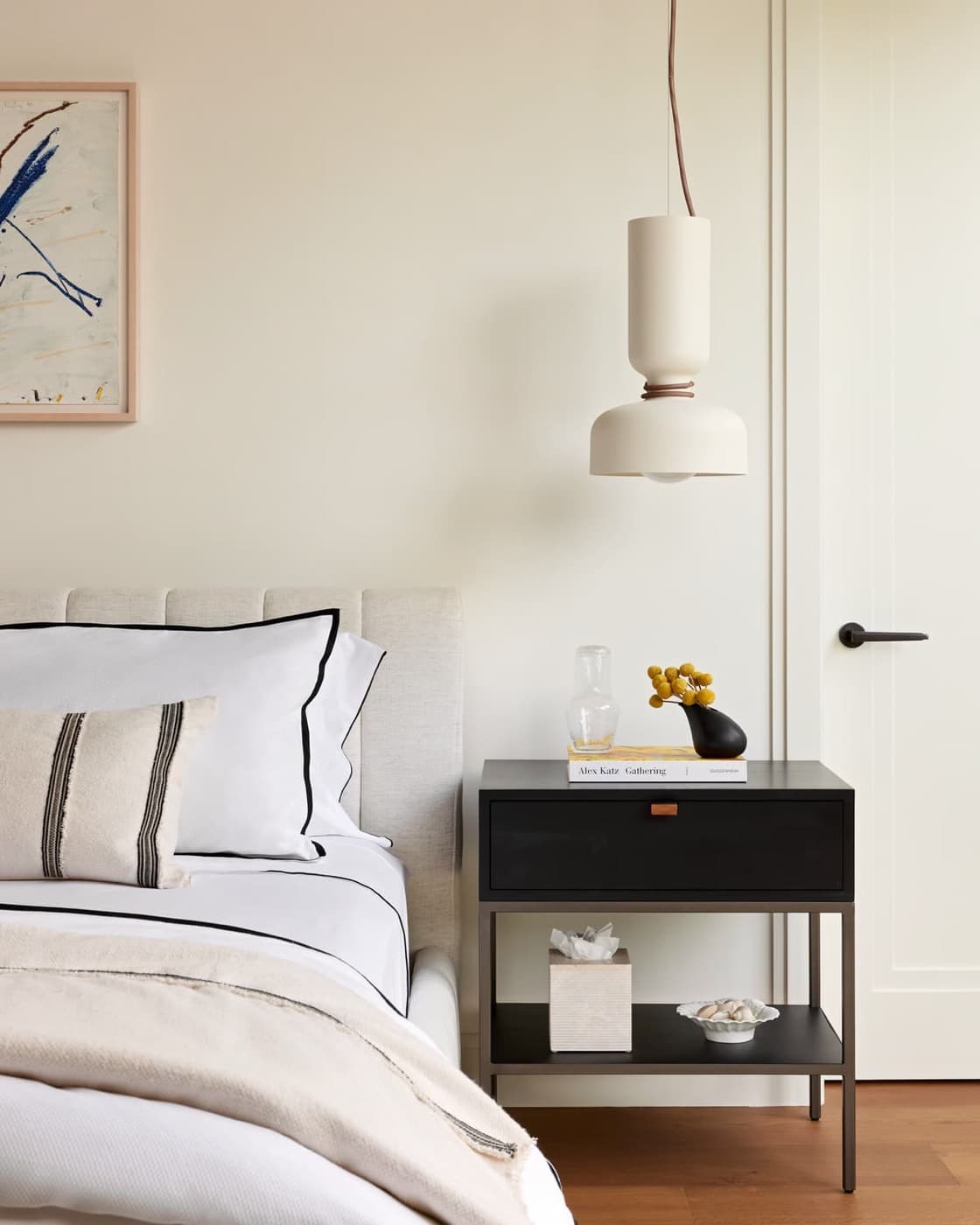 Bedroom with an upholstered bed, dark nightstand, and modern hanging pendant light