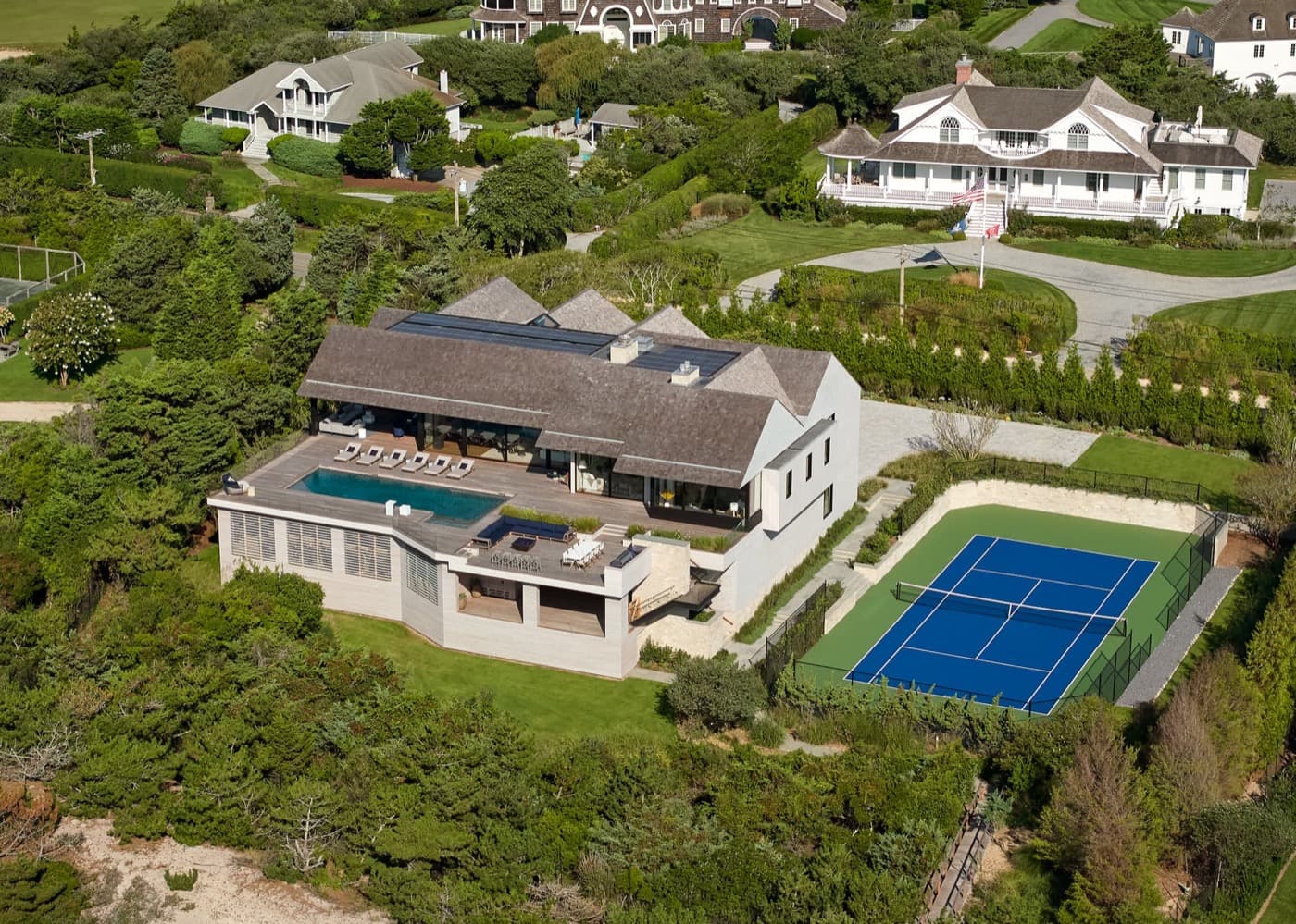 Aerial view of a coastal residence featuring an elevated swimming pool terrace and tennis court