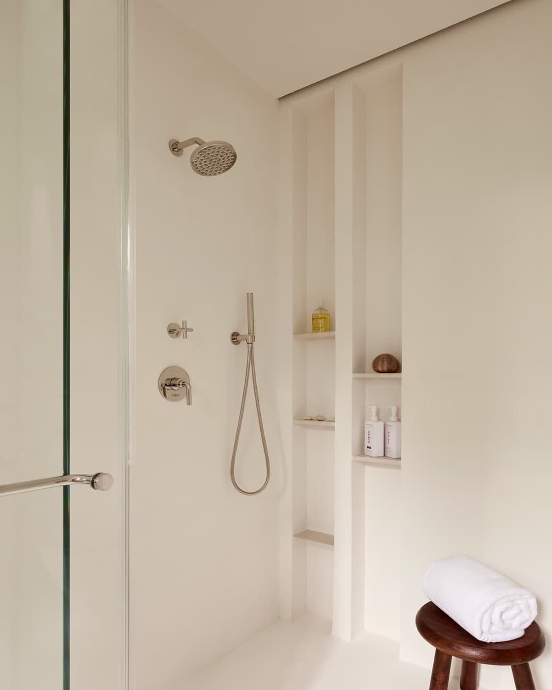 Minimalist walk-in shower featuring recessed vertical wall niches, metal fixtures, and glass enclosure
