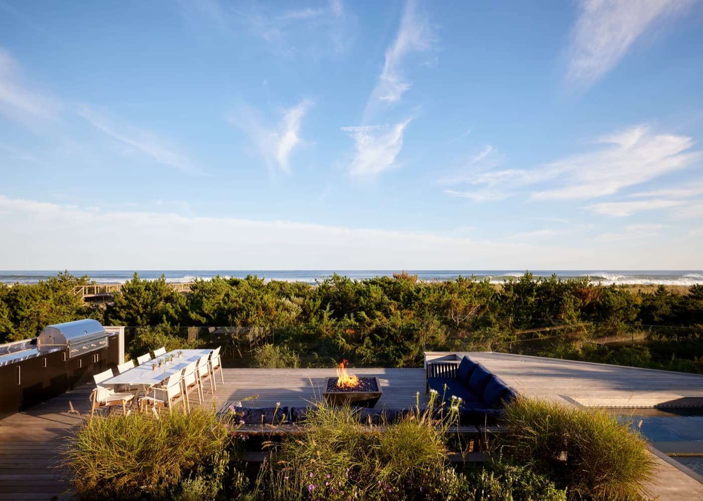 Oceanfront timber deck featuring a built-in outdoor kitchen, fire pit, and dining area