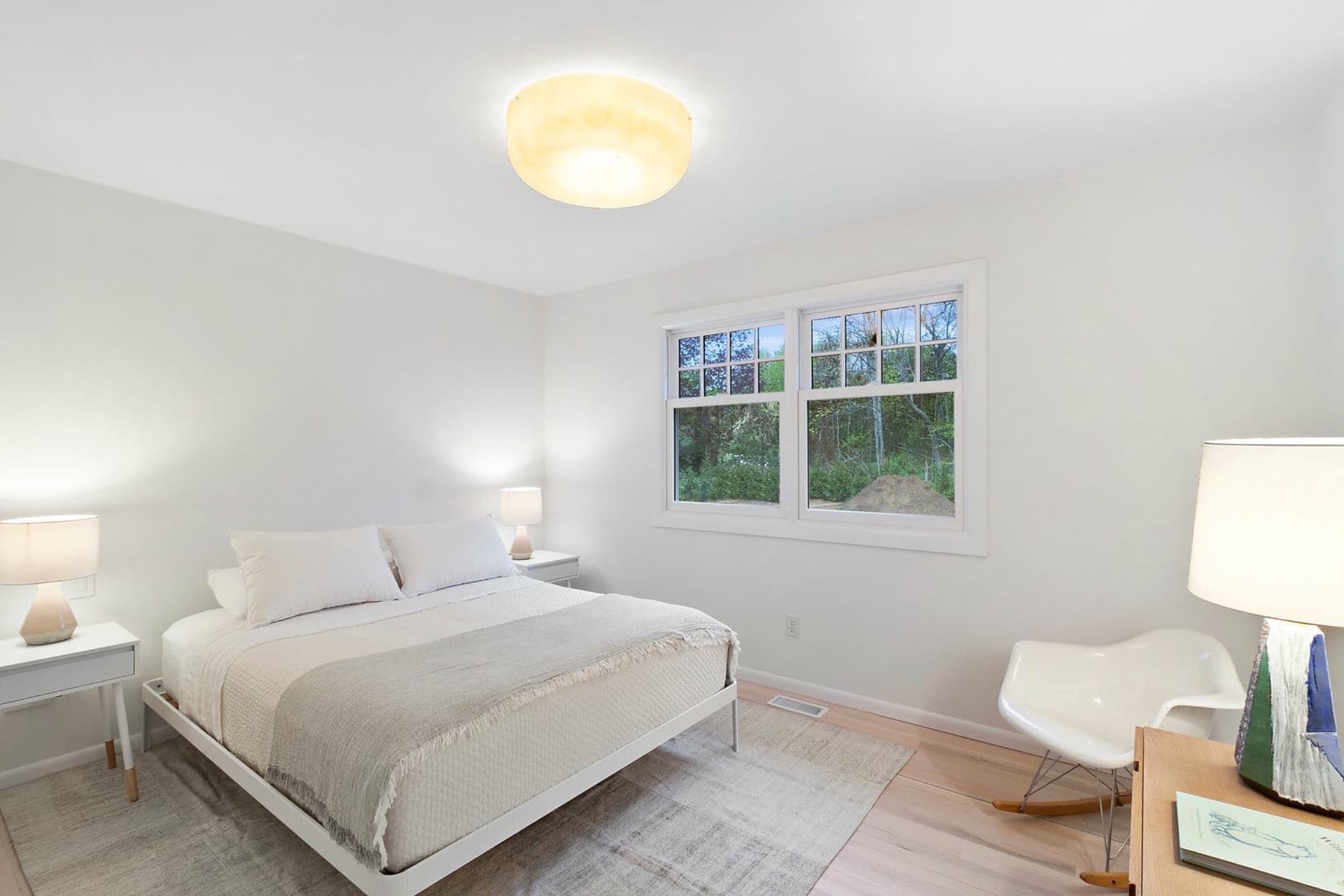 Bedroom featuring white-trimmed double windows, light timber flooring, and a glowing flush-mount ceiling light