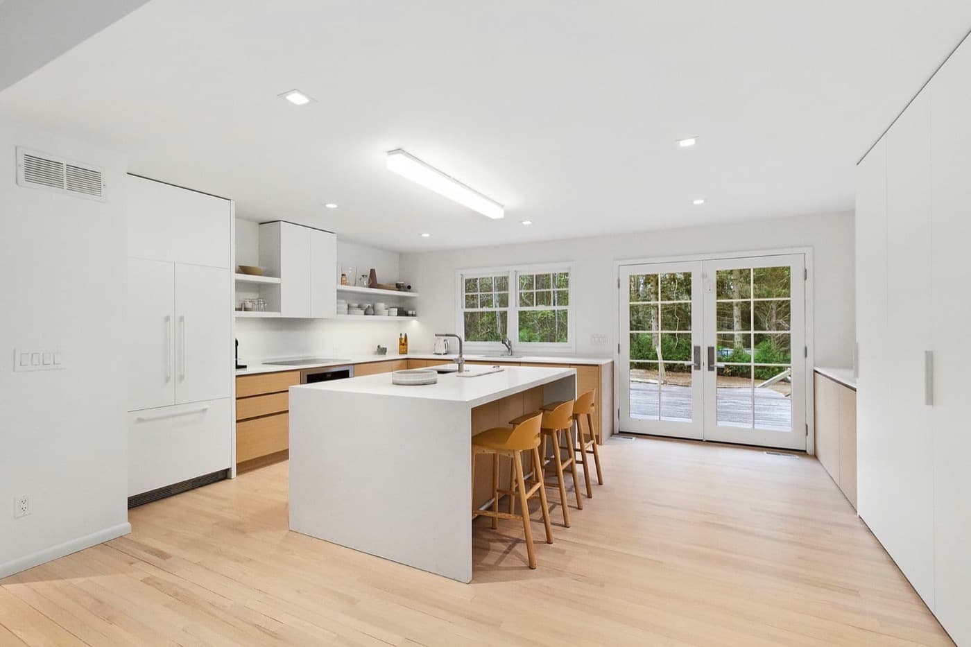 Modern kitchen with white waterfall island, light timber cabinetry, integrated storage, and French doors