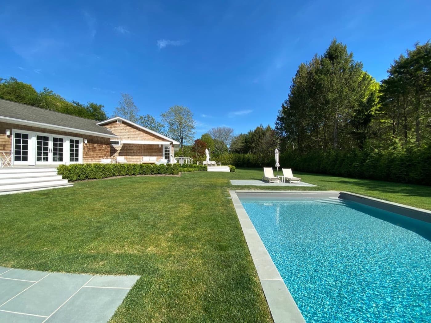 Backyard with a stone-bordered swimming pool, manicured lawn, and shingle-clad house