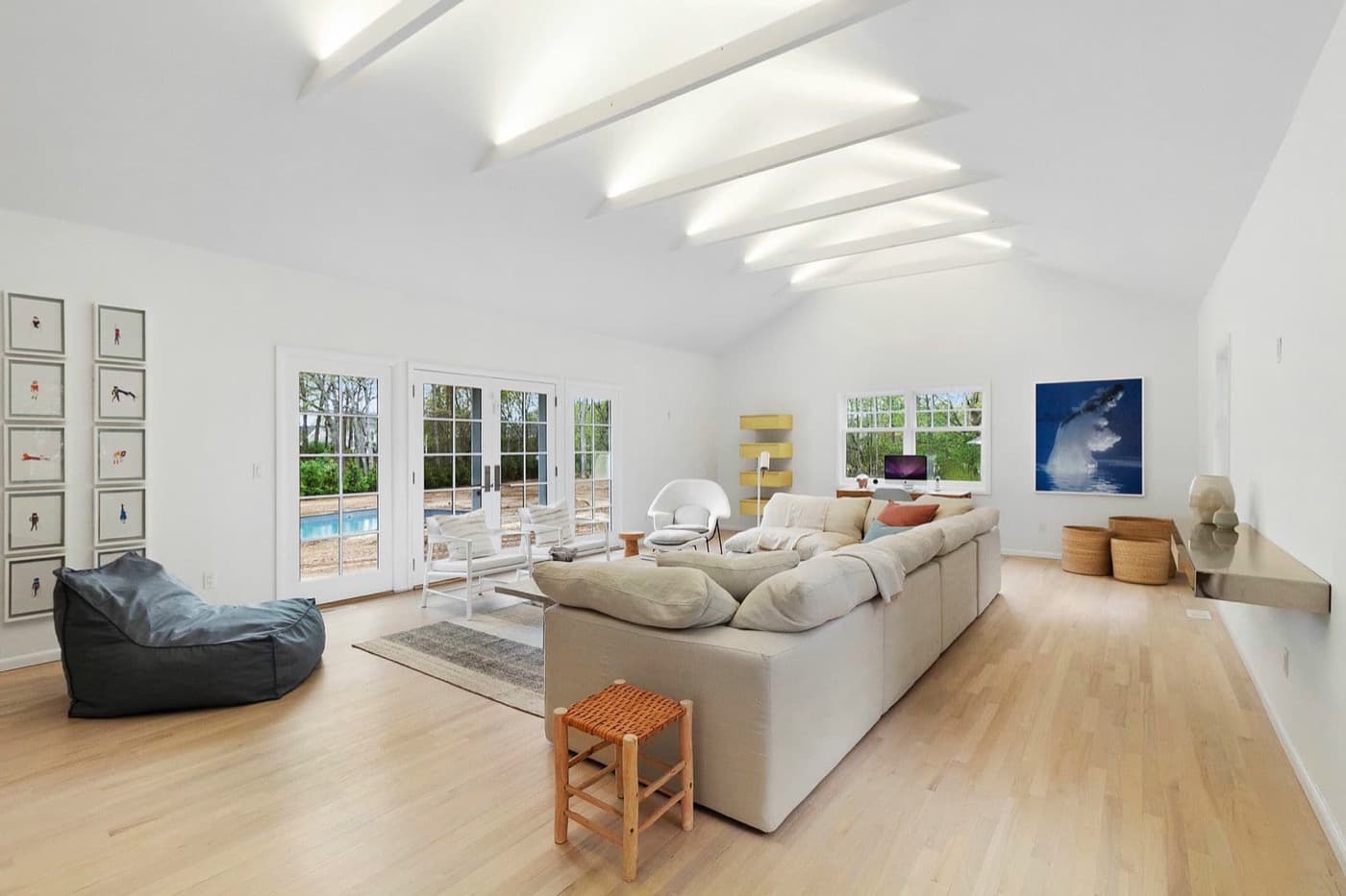 Open living room with illuminated ceiling beams, pale timber flooring, and white French doors