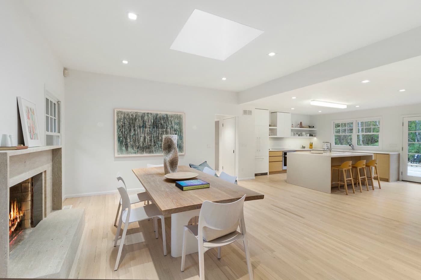Open-plan dining and kitchen space with a pale stone fireplace and kitchen island cabinetry