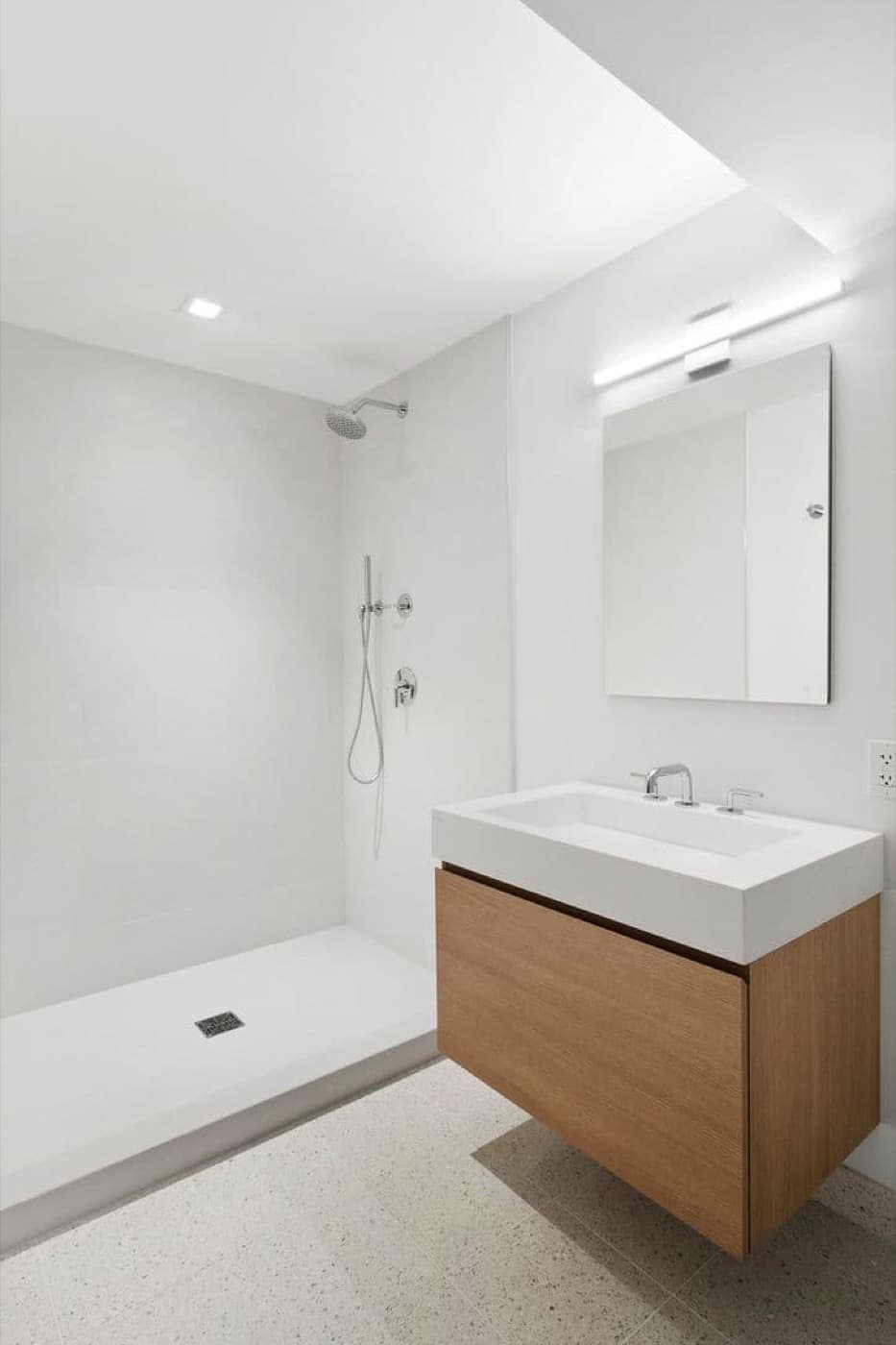 Minimalist bathroom with a floating oak-toned vanity, integrated white basin, and walk-in shower