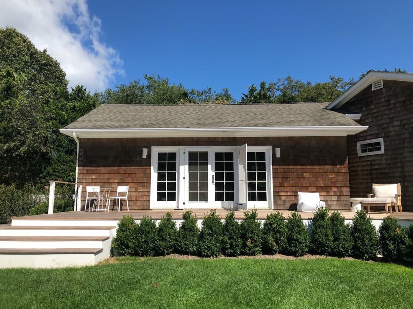 Exterior backyard patio featuring timber deck steps and shingled cottage with white French doors