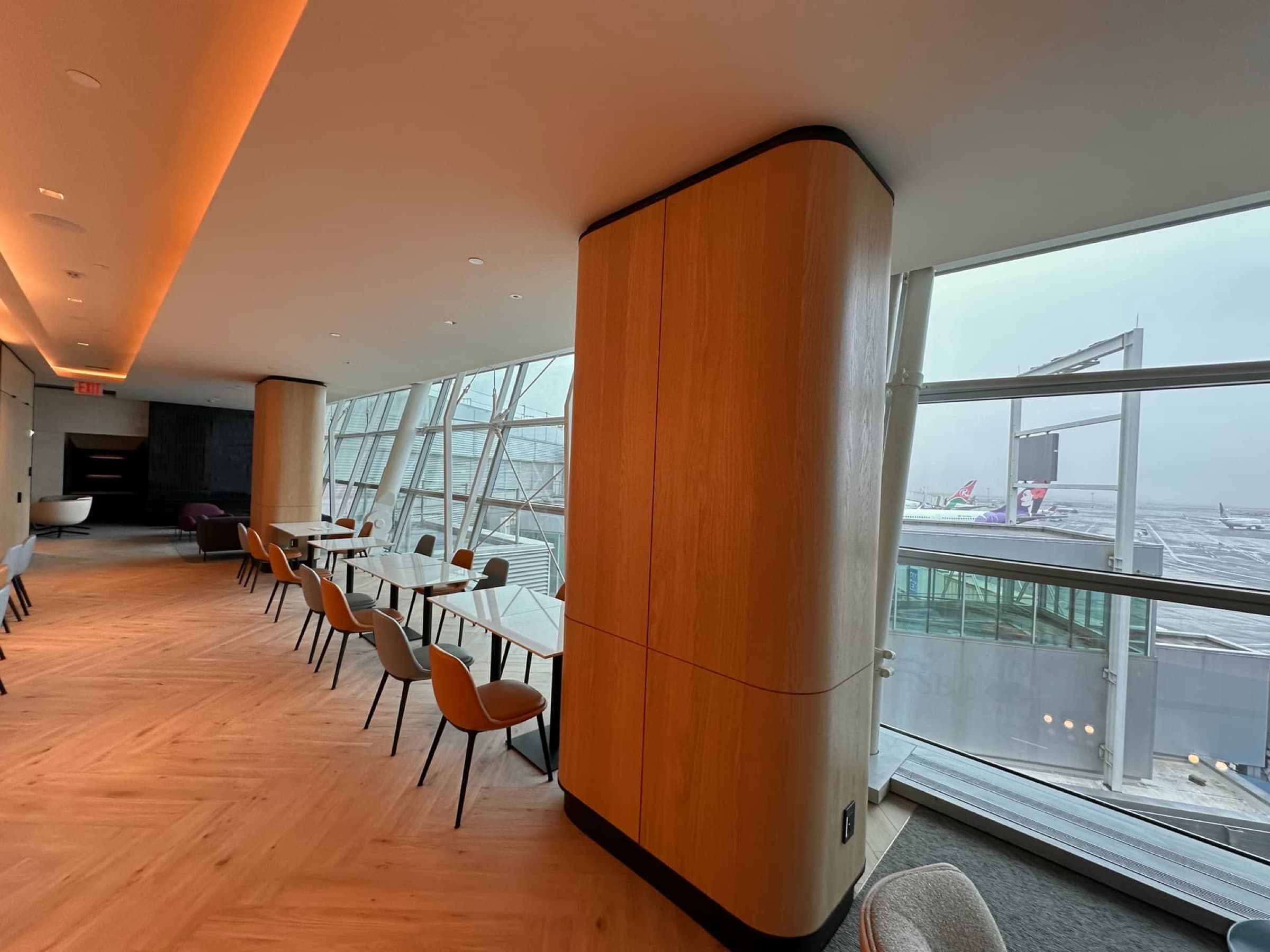 Airport lounge with curved timber-clad columns, herringbone timber flooring, and tables along floor-to-ceiling windows