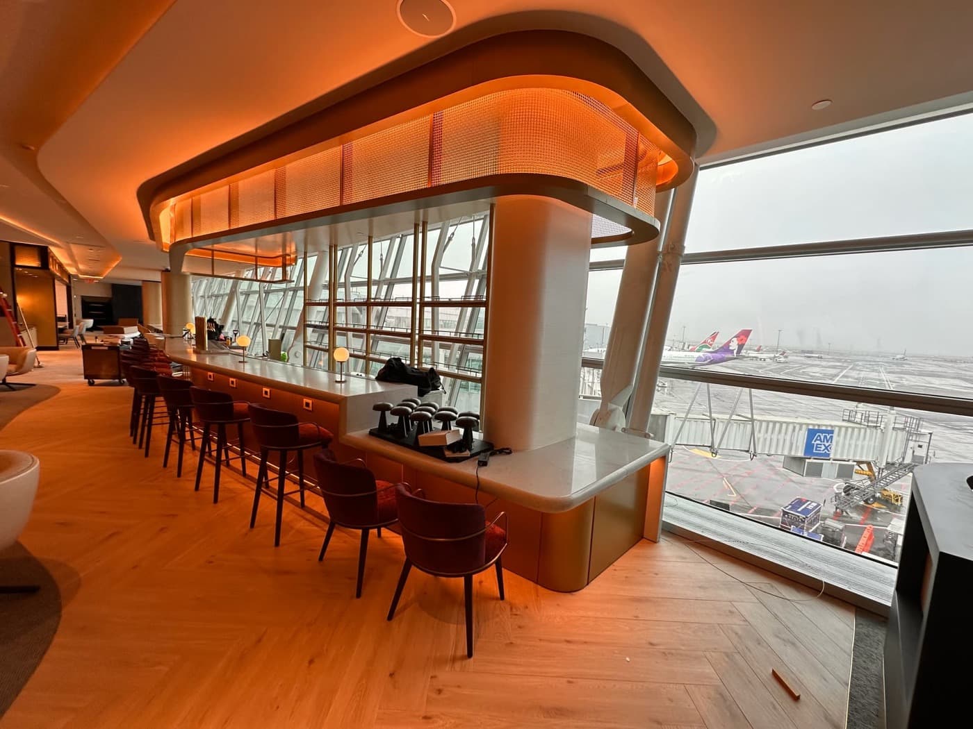 Airport lounge featuring a curved bar counter, backlit ceiling canopy, and herringbone timber flooring