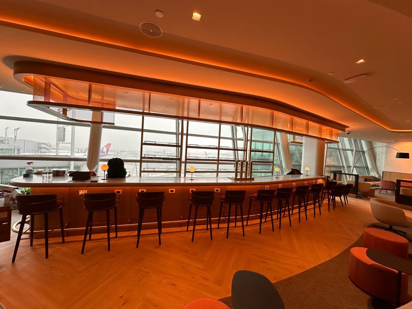 Airport lounge featuring a curved bar counter with illuminated overhead canopy and timber flooring