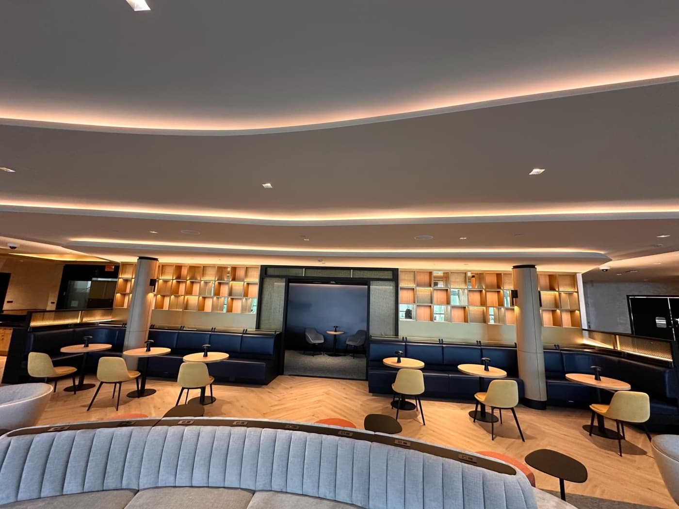 Commercial lounge with curved cove-lit ceiling above built-in banquettes and illuminated wall shelving
